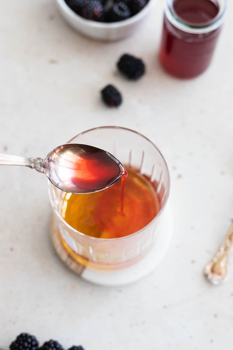 Blackberry simple syrup pouring from a spoon into the glass. 