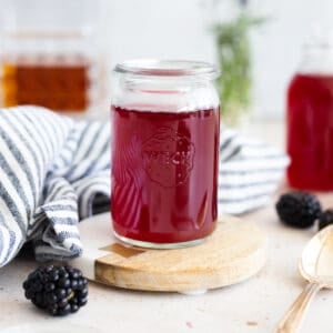 Blackberry simple syrup in a small glass jar with a blue and white striped linen.