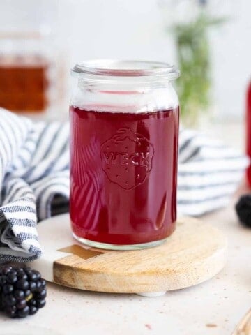 Blackberry simple syrup in a small glass jar with a blue and white striped linen.