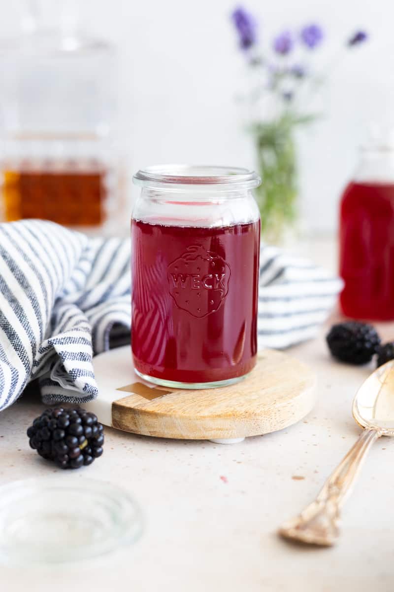 Blackberry simple syrup in a small glass jar with a stripped blue and white napkin. 