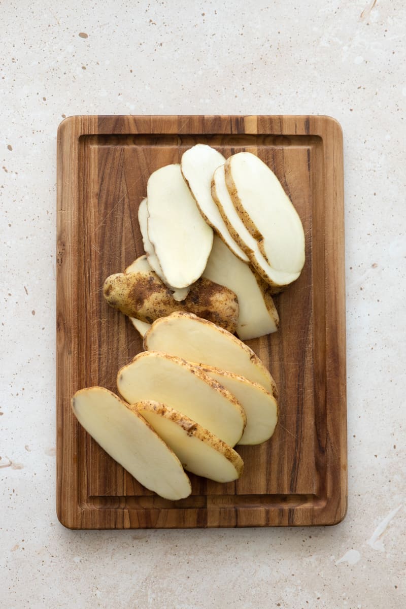 Potatoes cut into "disks" on a wooden cutting board. 