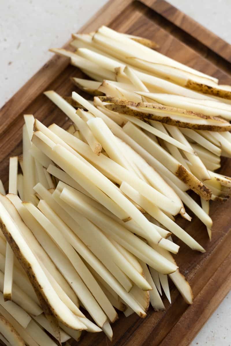 Potatoes sliced into matchstick fries on a wooden cutting board.