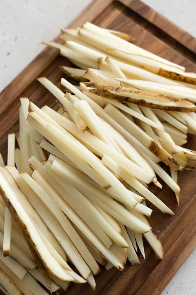 Potatoes sliced into matchstick fries on a wooden cutting board. 