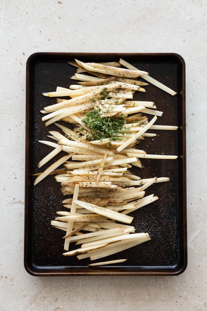 Fries on a baking sheet sprinkled with olive oil, herbs and spices.