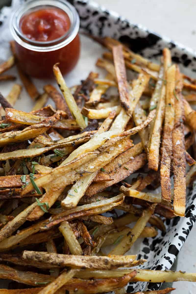 A closeup of garlic rosemary fries on a tray with a small bowl of ketchup. 