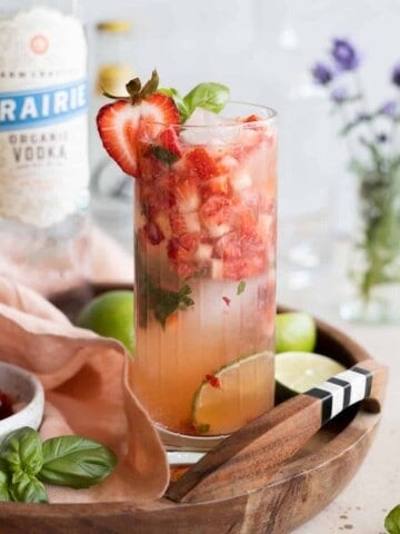 Closeup of a strawberry basil vodka cocktail on a wooden tray.