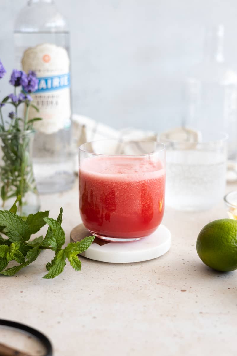 Watermelon juice in a glass surrounded by mint and limes. 