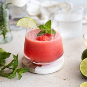 A watermelon mint cocktail in a rocks glass garnished with mint and a lime slice.