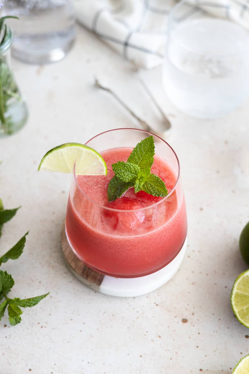 A watermelon mint cocktail garnished with a lime slice and mint sprig. 