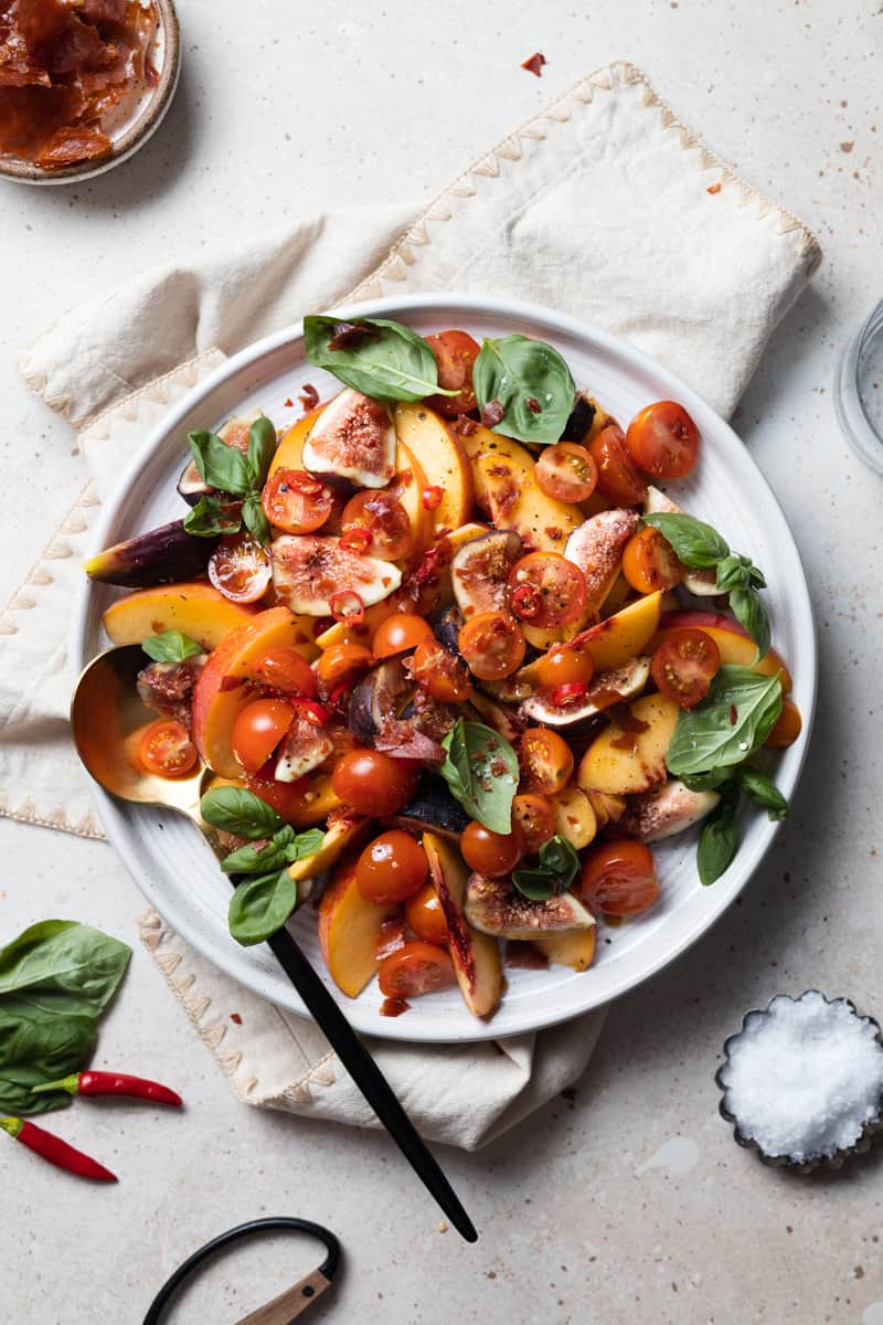 Peach and Prosciutto Salad on a white platter with a black and gold serving spoon. 