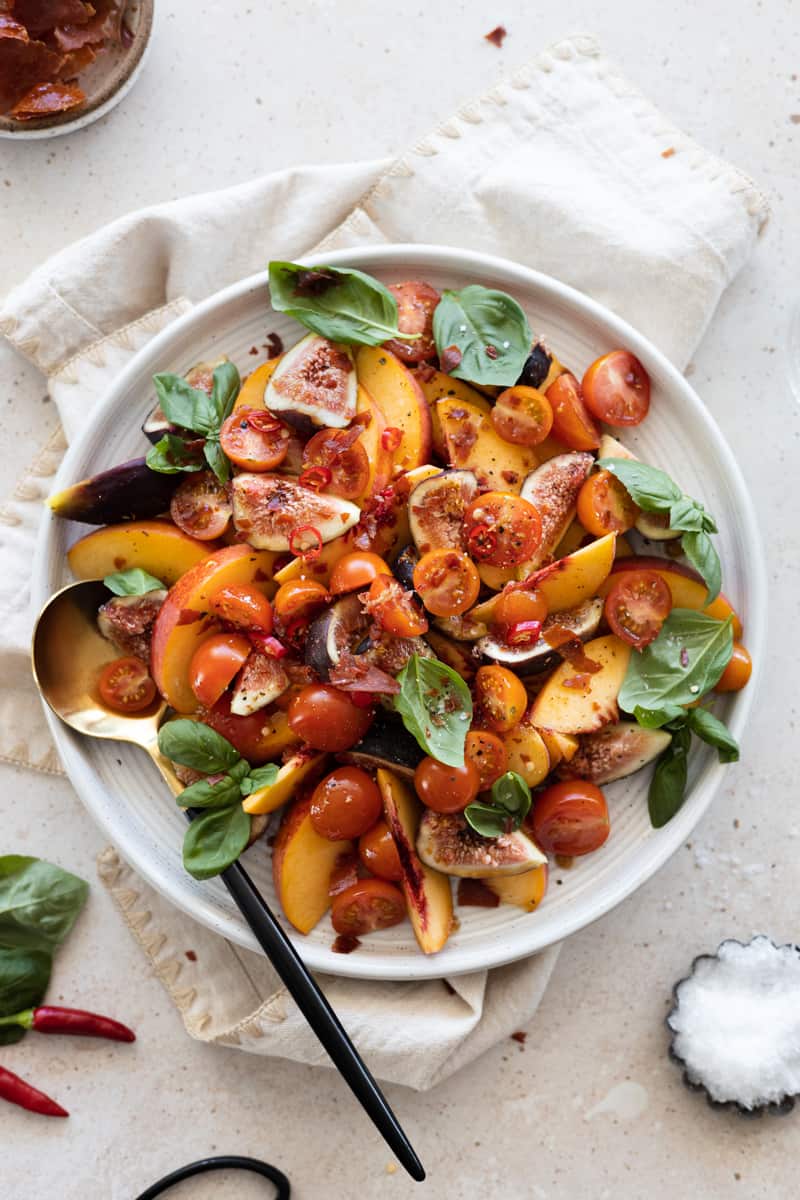 Final Peach and Prosciutto Salad on a white platter, topped with fresh basil and crumbled prosciutto. 