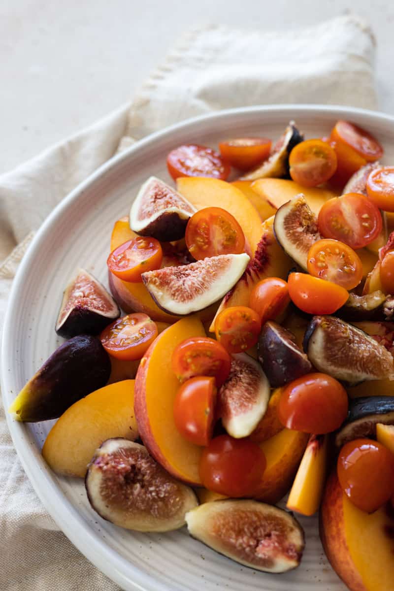 Sliced peaches, figs and cherry tomatoes on a white platter. 