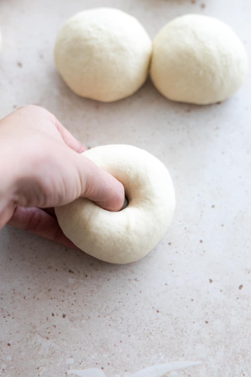 A thumb pressing a hole through the center of the dough ball to create the bagel shape. 
