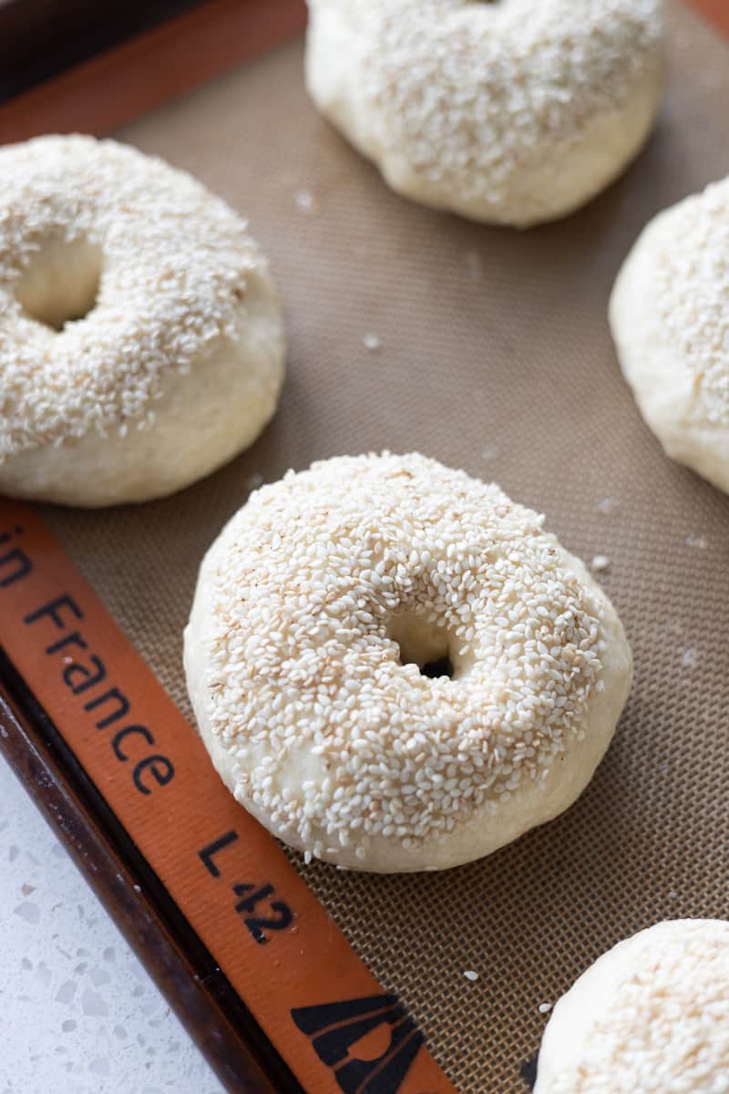 Bagels on a baking tray covered in sesame seed toppings. 