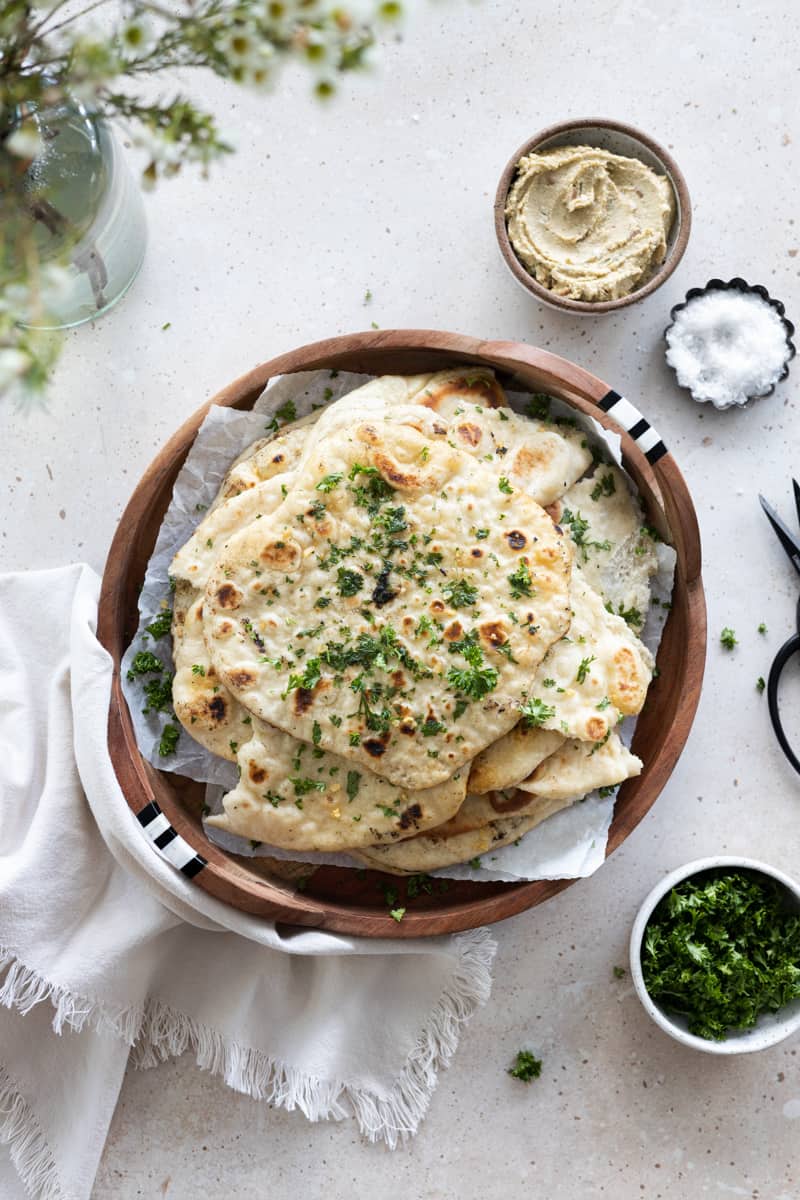 Sourdough discard naan in a pile on a wooden tray.