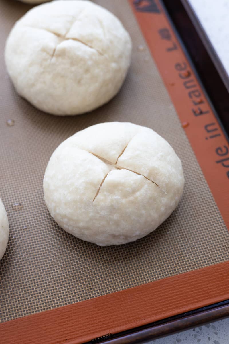 Scored buns on a baking sheet. 