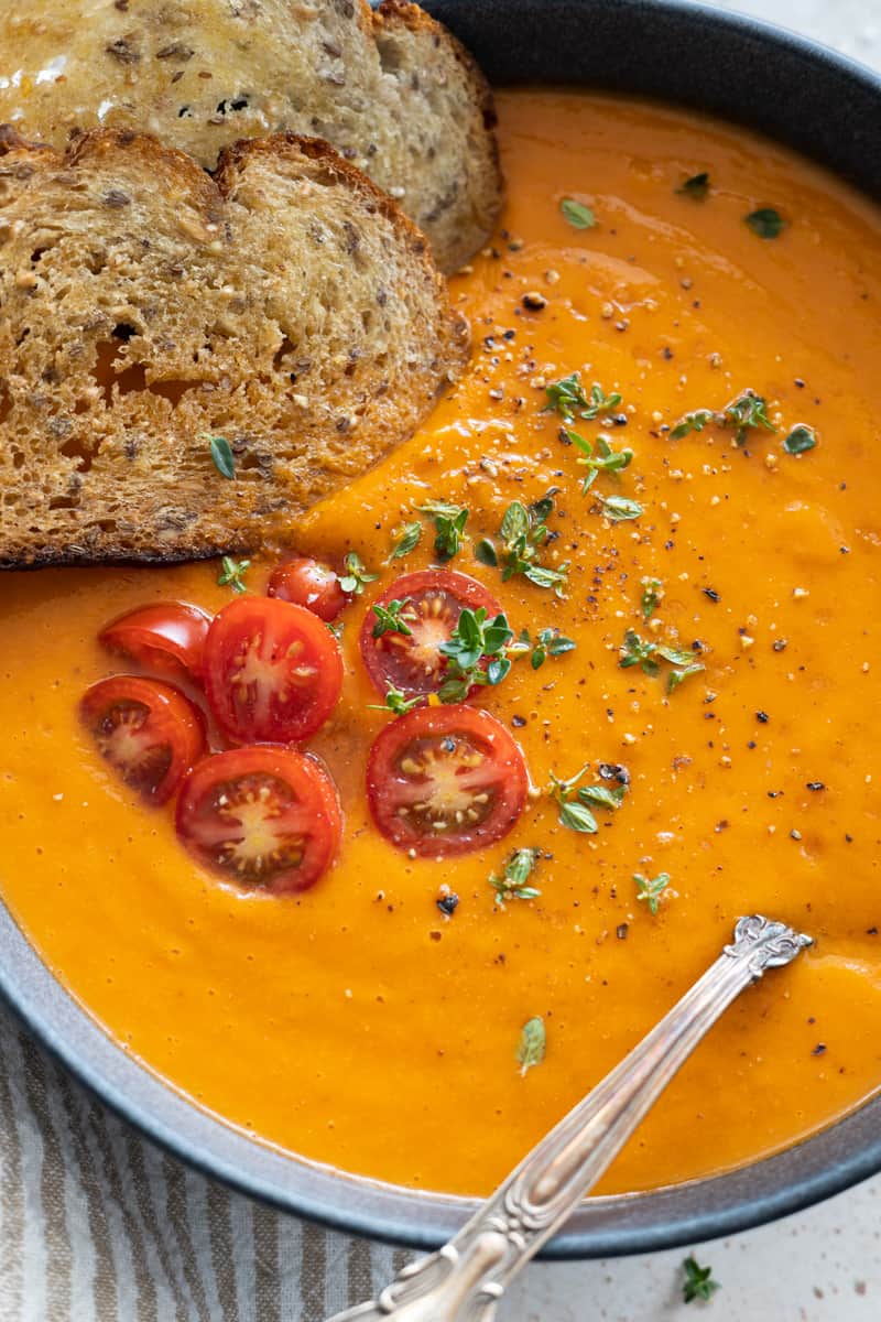 Closeup of the toppings on the soup: crusty bread, halved cherry tomatoes, fresh thyme, salt and pepper.