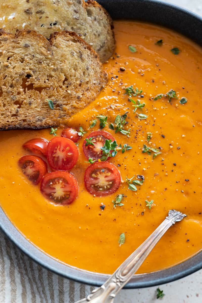 Closeup of the toppings on the soup: crusty bread, halved cherry tomatoes, fresh thyme, salt and pepper. 