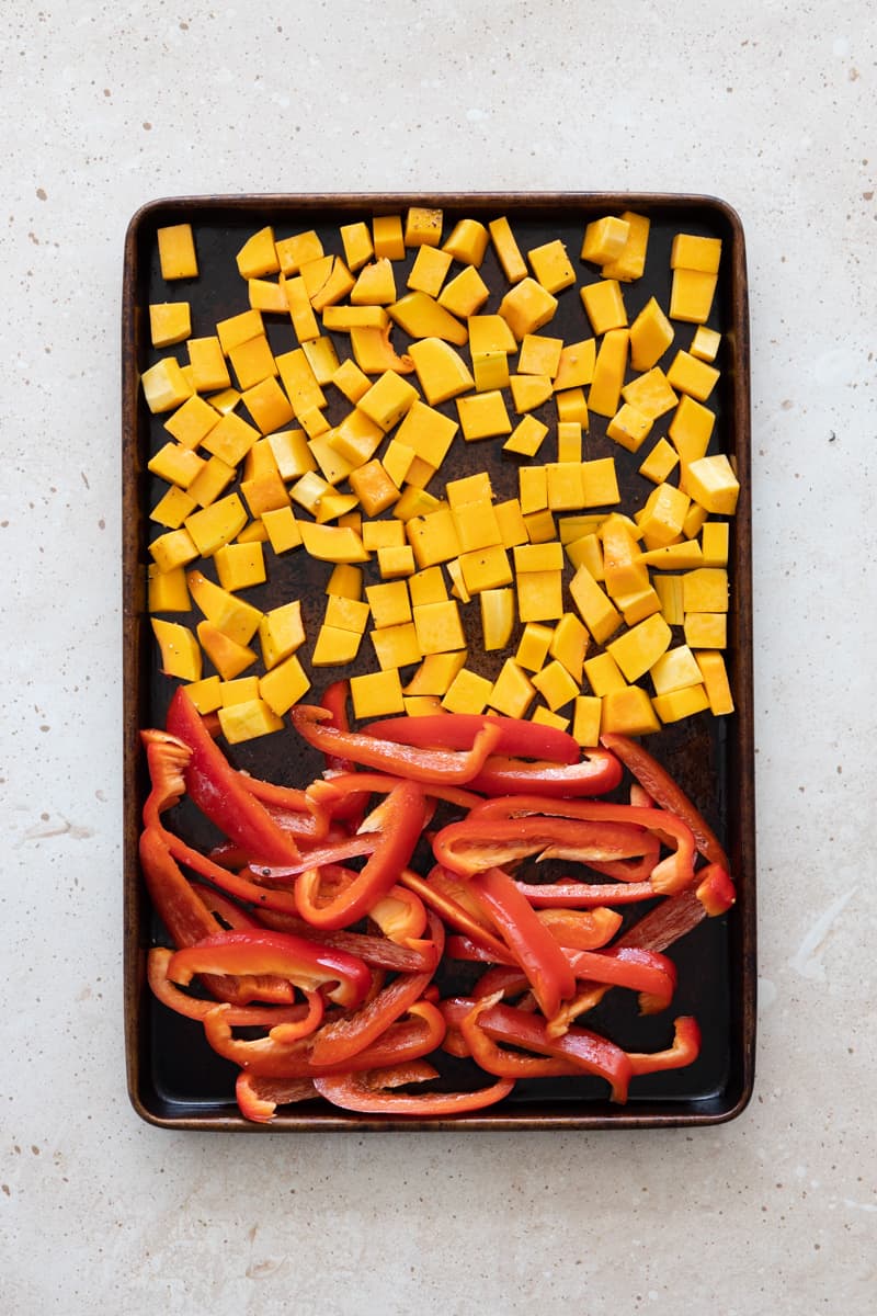 Butternut squash and red peppers chopped and spread on a baking sheet.