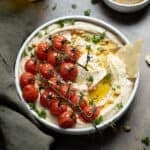 Hummus with vine roasted tomatoes in a white bowl.