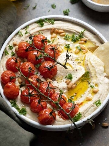 Hummus with vine roasted tomatoes in a white bowl.