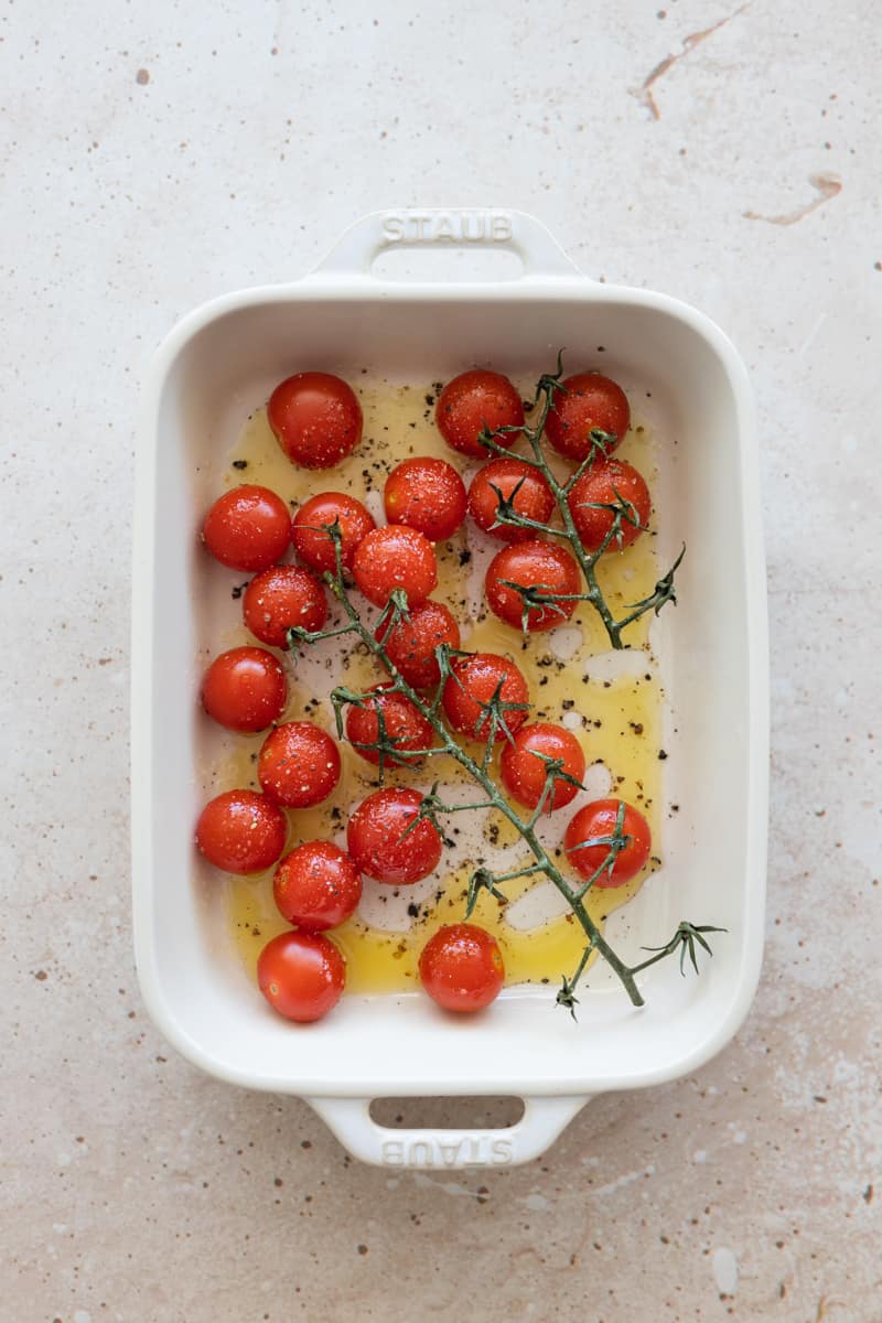 Tomatoes on the vine in a white baking dish. 