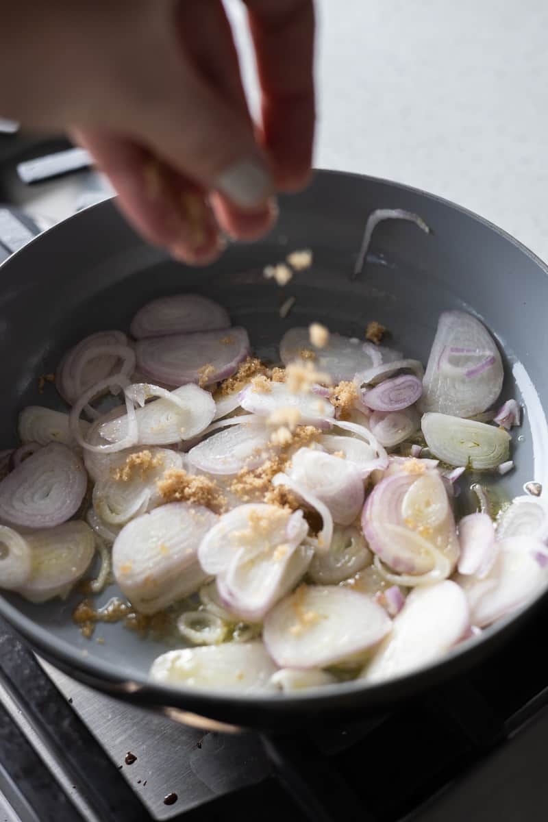 Sliced shallots in a small skillet being sprinkled with brown sugar. 