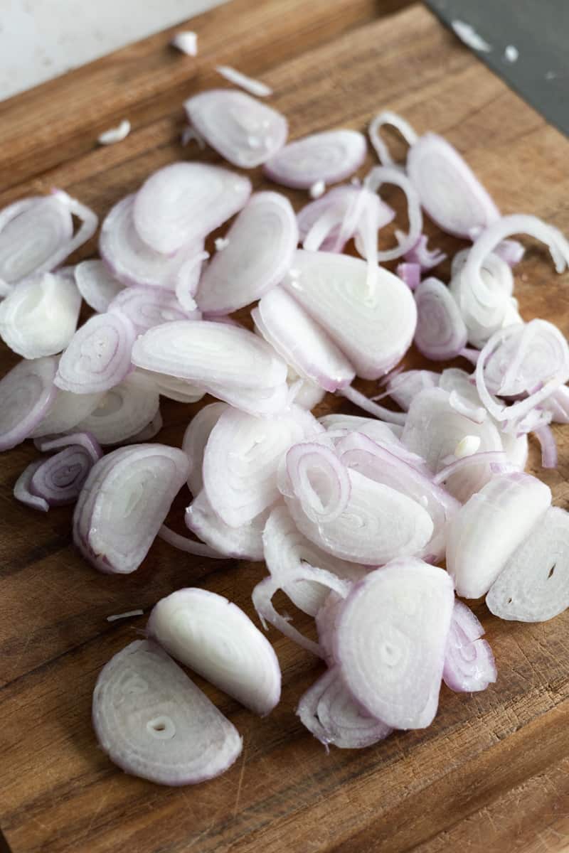 Sliced shallots on a wooden cutting board. 