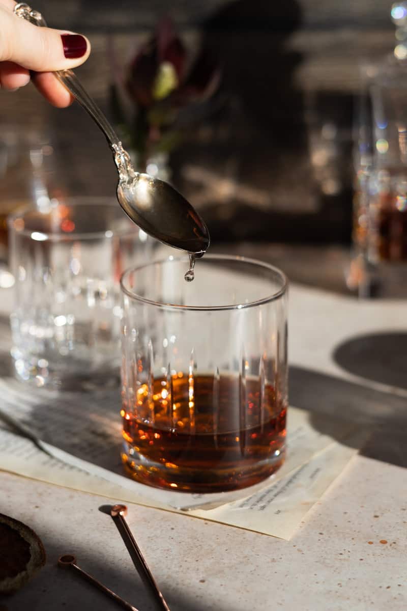 Simple syrup being added from a spoon to the bourbon glass. 