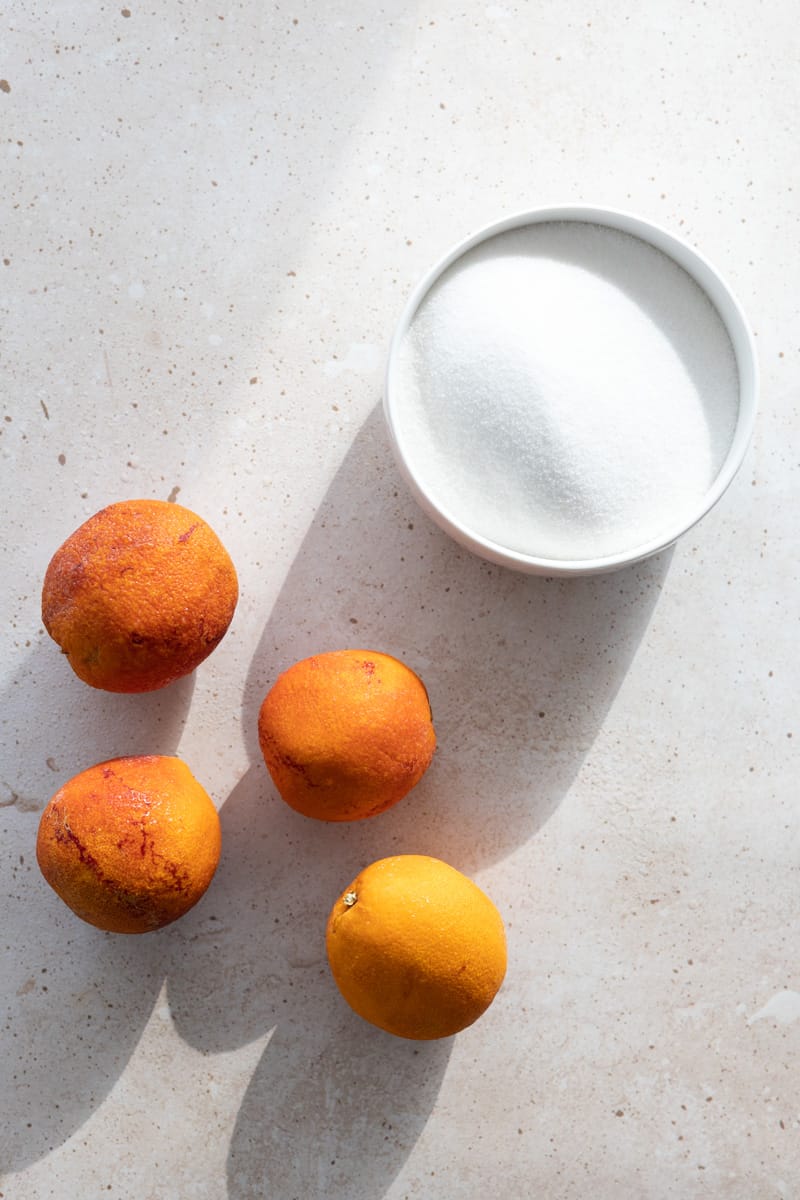 Blood oranges and a bowl of sugar on a countertop.