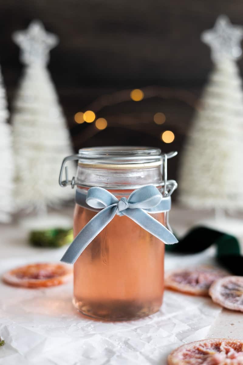 A jar of blood orange simple syrup tied with a blue ribbon. 