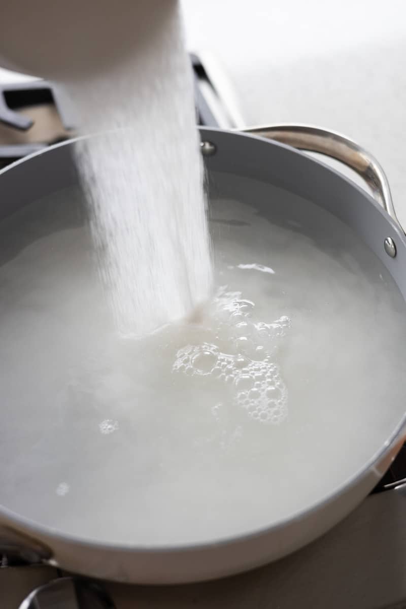 Sugar being poured into a large pot of water. 