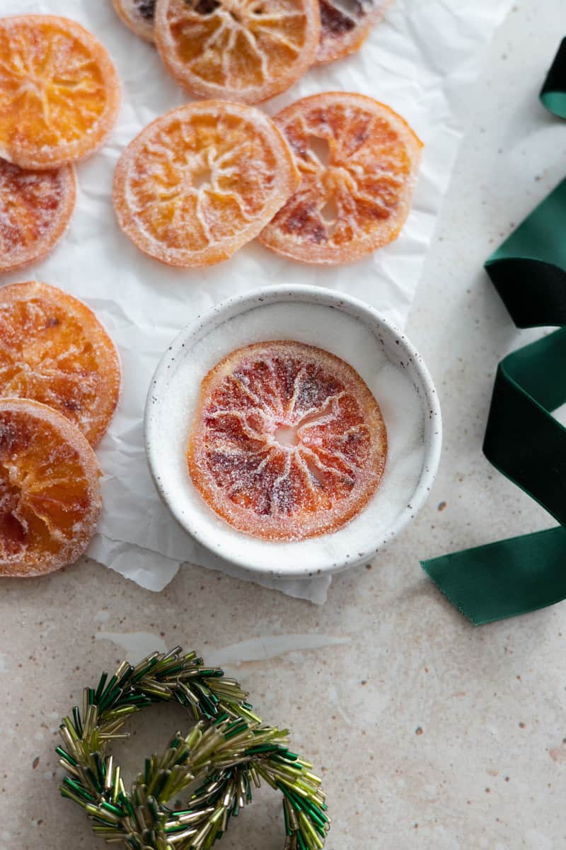 Oranges being coated in a small bowl of sugar. 