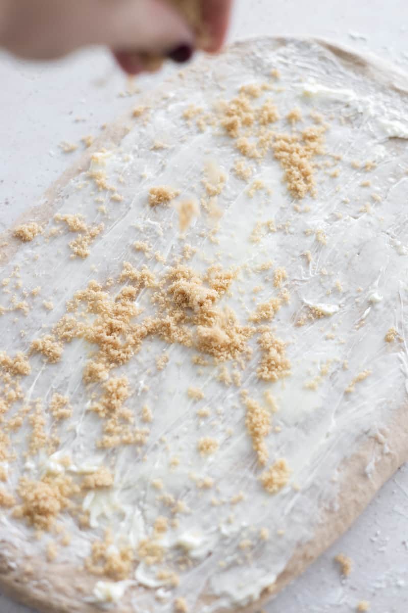 Dough spread with butter and being sprinkled with brown sugar. 