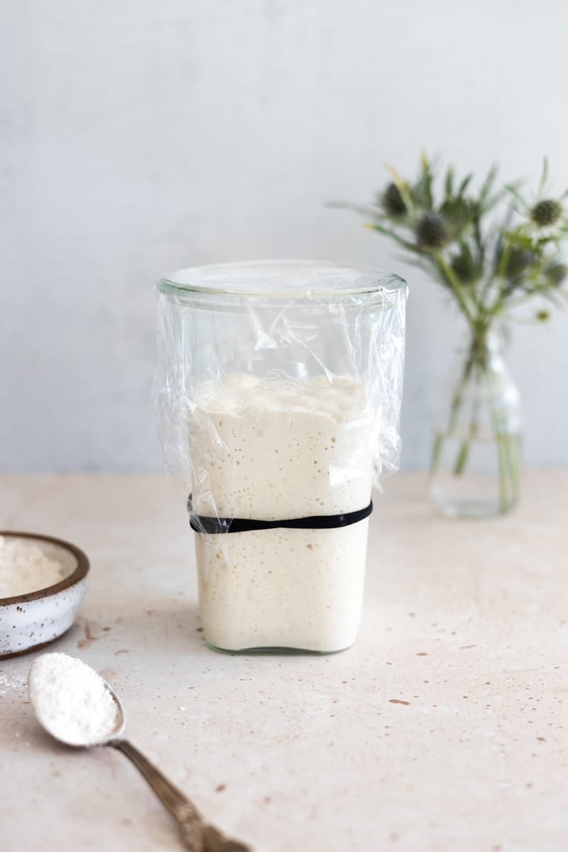 Sourdough starter in a glass jar covered with plastic wrap.