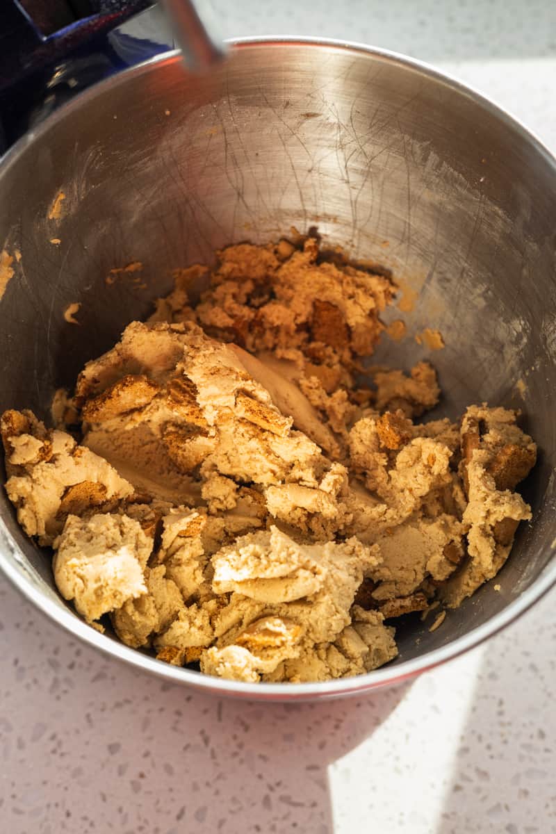 Cookie dough with cookie pieces mixed in the bowl of a stand mixer. 