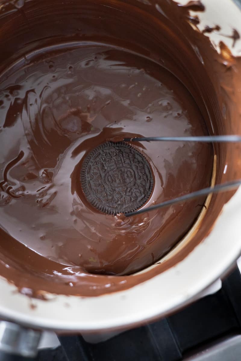 An oreo being dipped in the melted chocolate. 