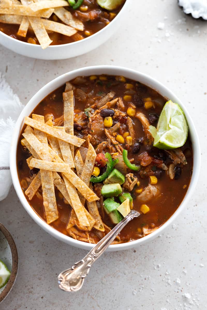 Bowl of healthy chicken tortilla soup topped with tortilla strips and a lime wedge. 