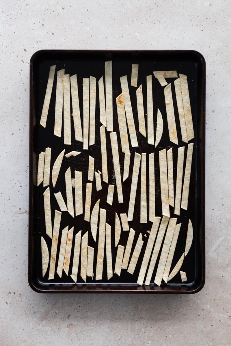 Tortilla strips spread on a baking sheet. 