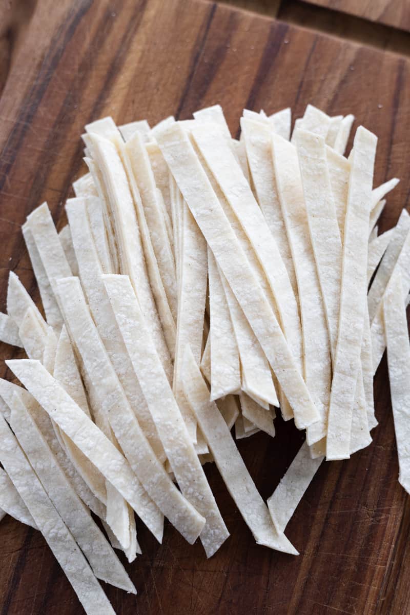 Tortilla strips cut into ¼-inch slices on a wooden cutting board. 