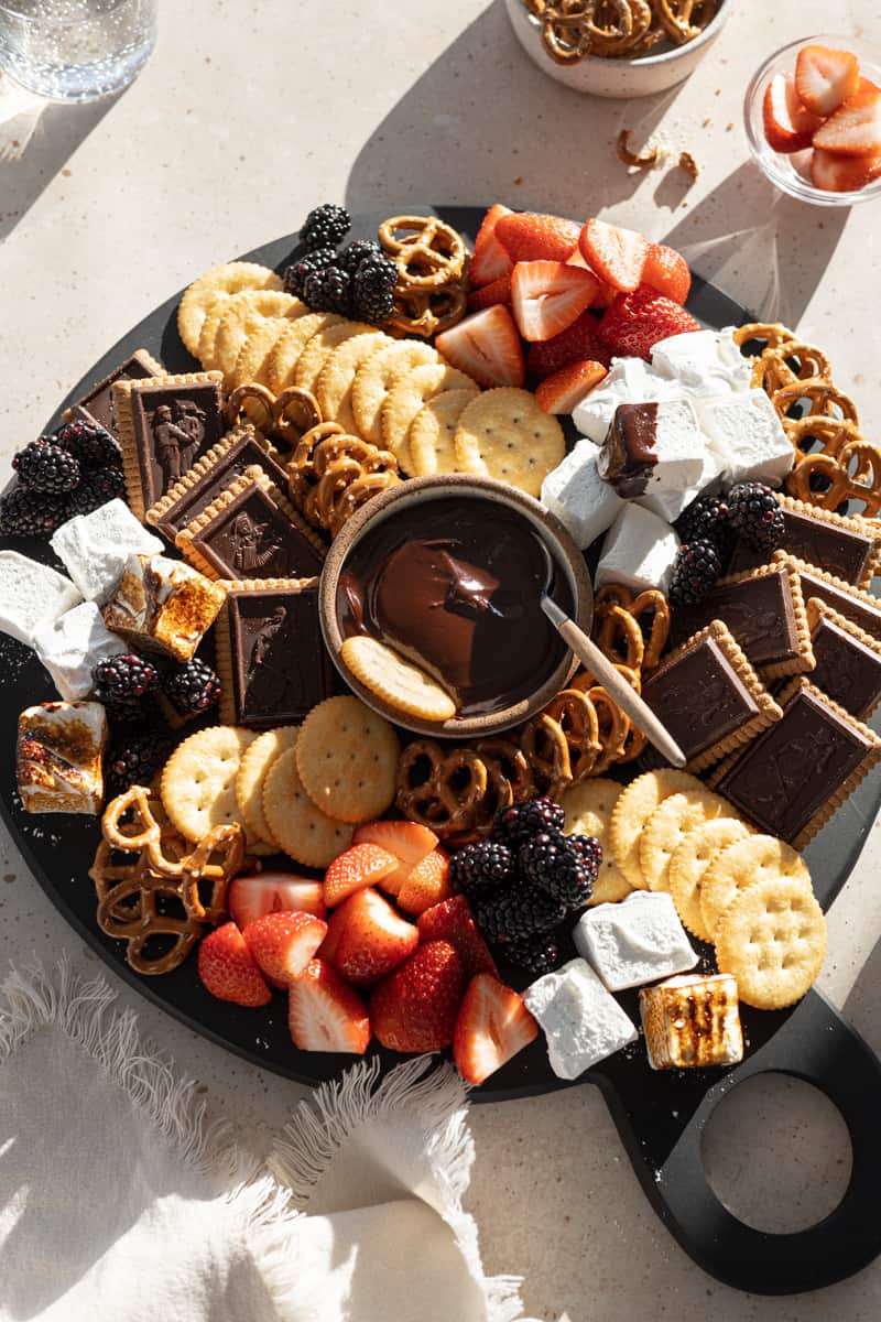 A full Dessert Charcuterie Board with a bowl of chocolate dipping sauce in the middle.