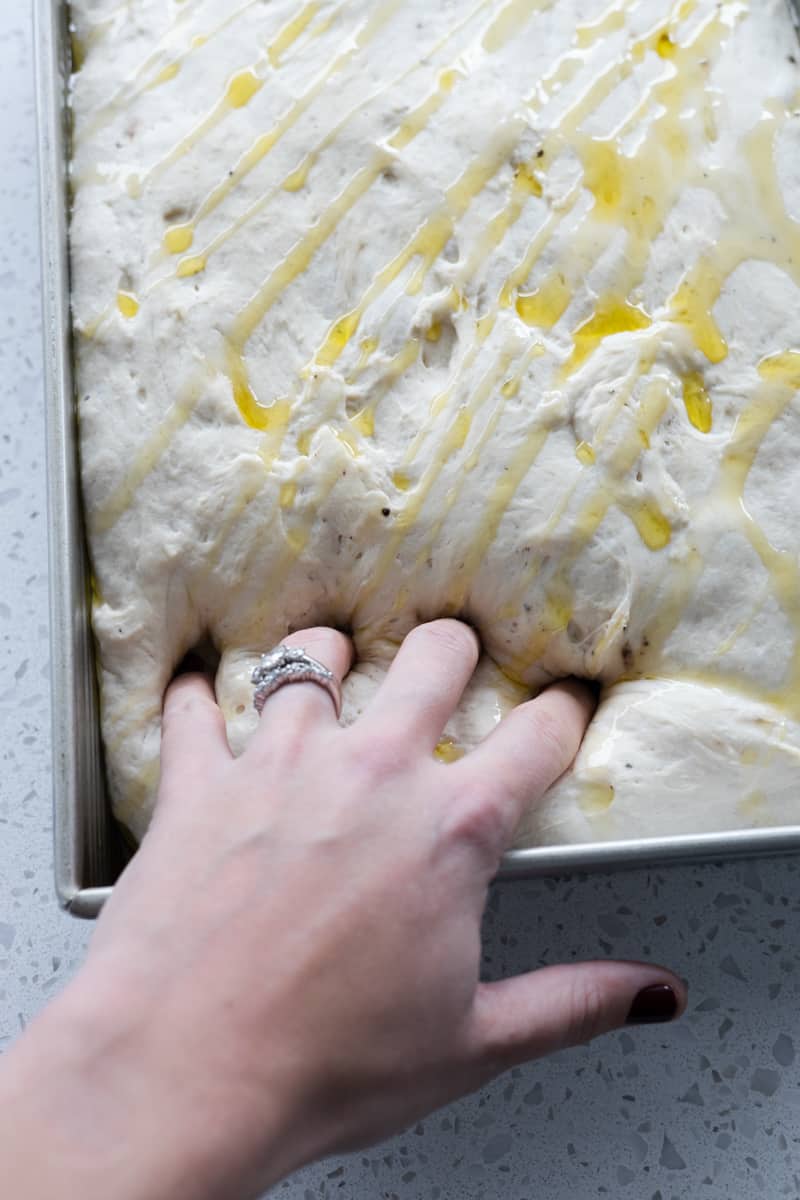 A hand pressing dimples into dough in the pan.