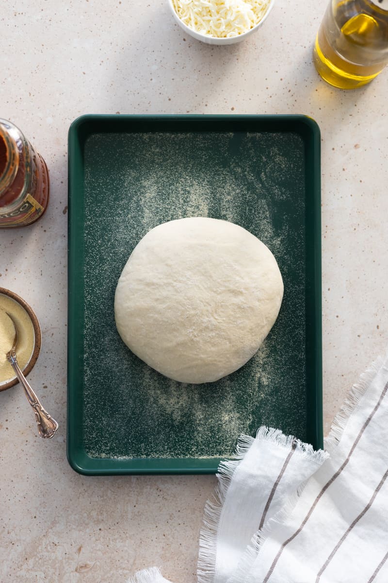 Sourdough discard pizza dough in a round on a green baking sheet.
