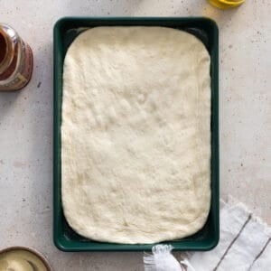 Sourdough discard pizza dough shaped on a green baking sheet.