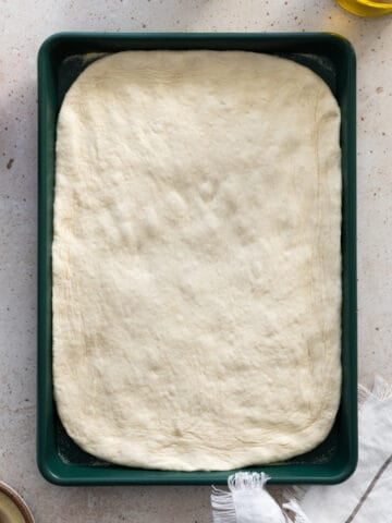 Sourdough discard pizza dough shaped on a green baking sheet.