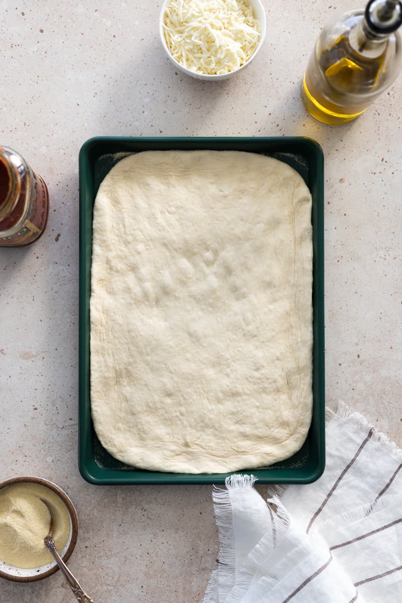 Sourdough discard pizza dough shaped on a green baking sheet.