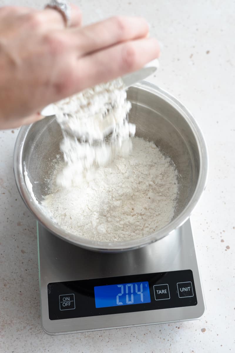 Flour being added to the metal bowl on the kitchen scale. 