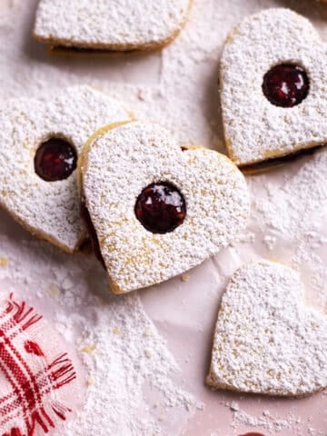 Heart Cookies with Jam stacked on a pink baking sheet.