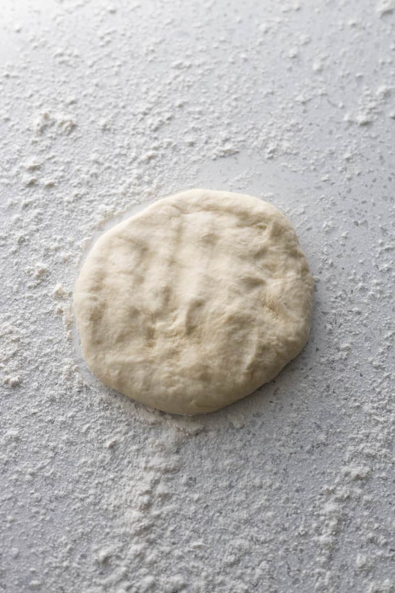 Dough flattened into a disk on a floured surface.