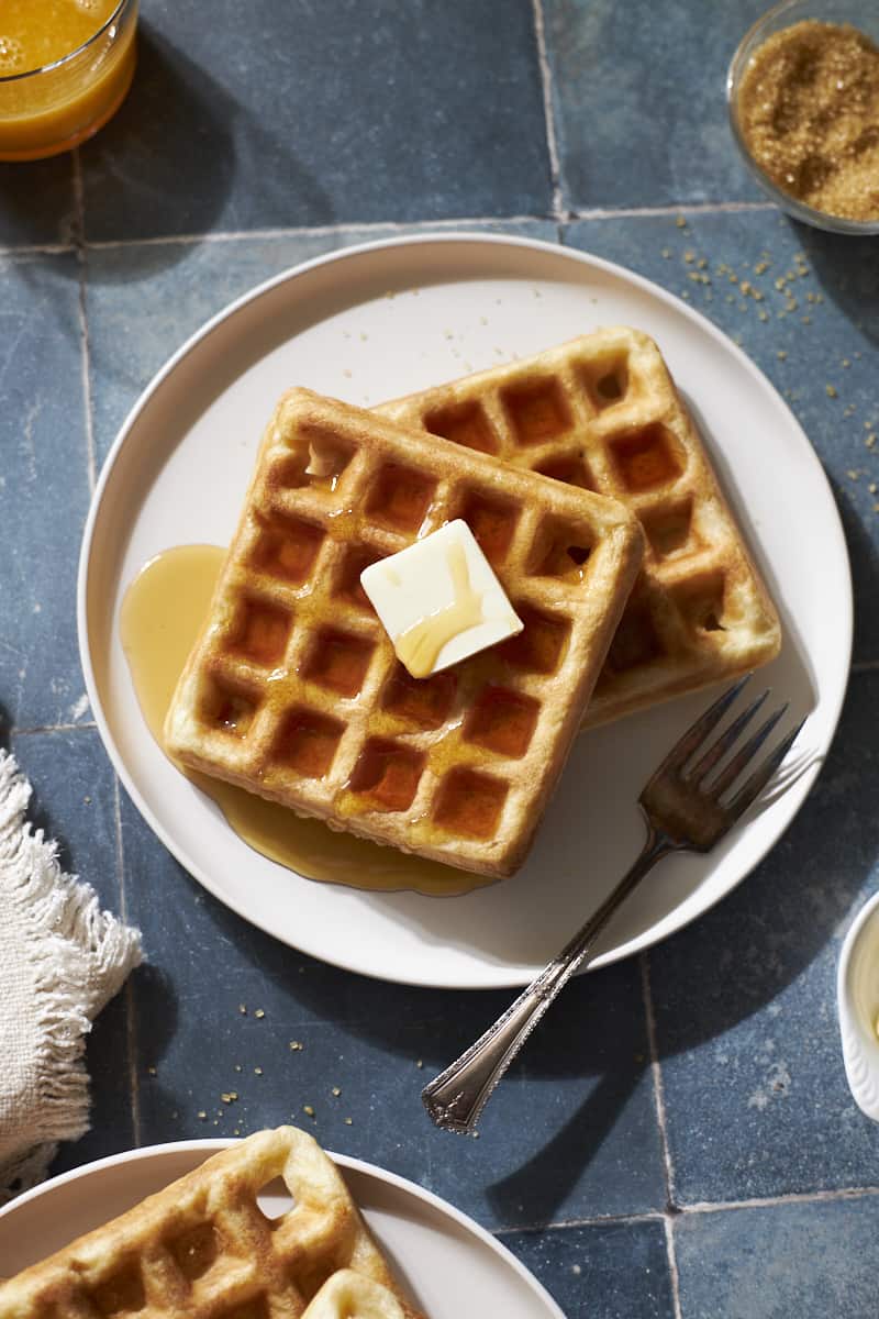 Two Sourdough Discard Waffles on a white plate with a pad of butter and maple syrup.